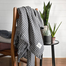Load image into Gallery viewer, Charcoal Hardy Houndstooth Cotton Throw Blanket draped on back of chair next to plants
