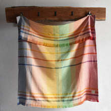 Load image into Gallery viewer, Rainbow design blanket hanging on a wooden rack against a white wall.