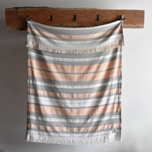 Load image into Gallery viewer, Orange, black, and white striped Amana Escape Cotton Throw hanging on a wooden rack against a gray background
