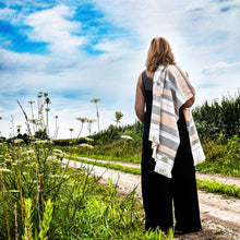 Load image into Gallery viewer, Person standing on a dirt path in a field with a striped blanket , looking towards a blue sky.